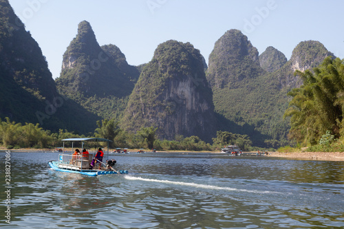 Raft on Li River in Guilin, China. Raft has 3 passengers, green limestone hills in the background, water in foreground.