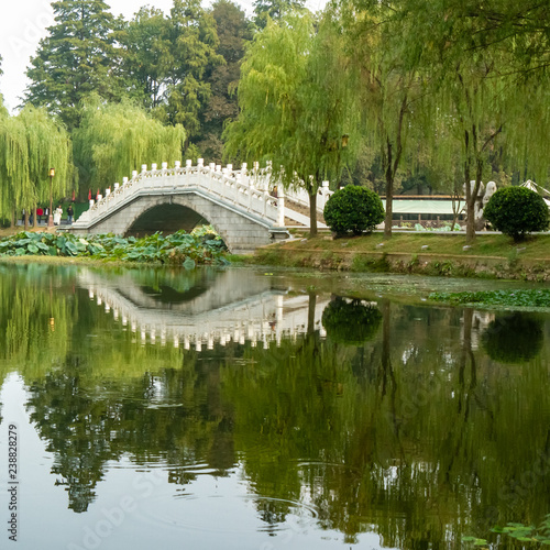 Bridge and surrounding tree reflected in water in East Lake, Wuhan, China. Crystal clear reflection on water of bridge and surrounding willow trees.