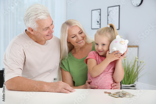 Foto Little girl with piggy bank and her grandparents at table
