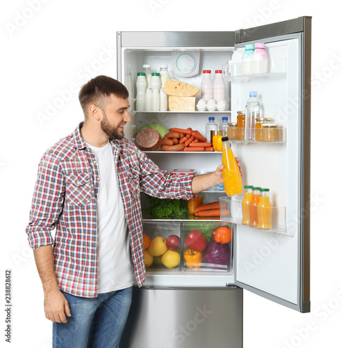 Young man taking bottle of juice from refrigerator on white background