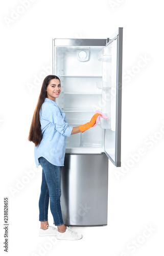 Young woman cleaning refrigerator with rag on white background