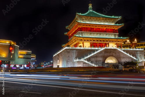 Bell Tower at night, Xian, China. Tower is lit up in sage green, soft yellow, and bright orange colors on top of a section of the old city wall.