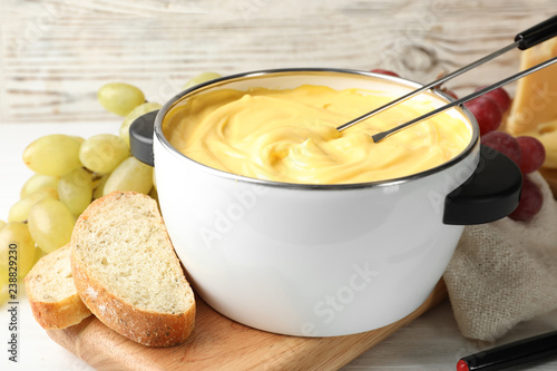 Pot with delicious cheese fondue and forks on wooden table