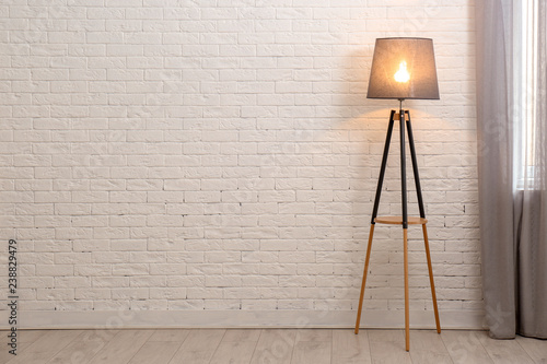 Modern floor lamp against brick wall indoors. Space for text photo
