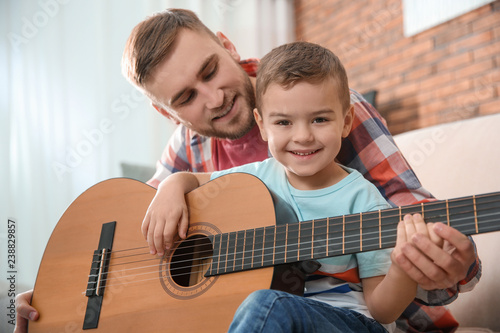 Father teaching his little son to play guitar at home