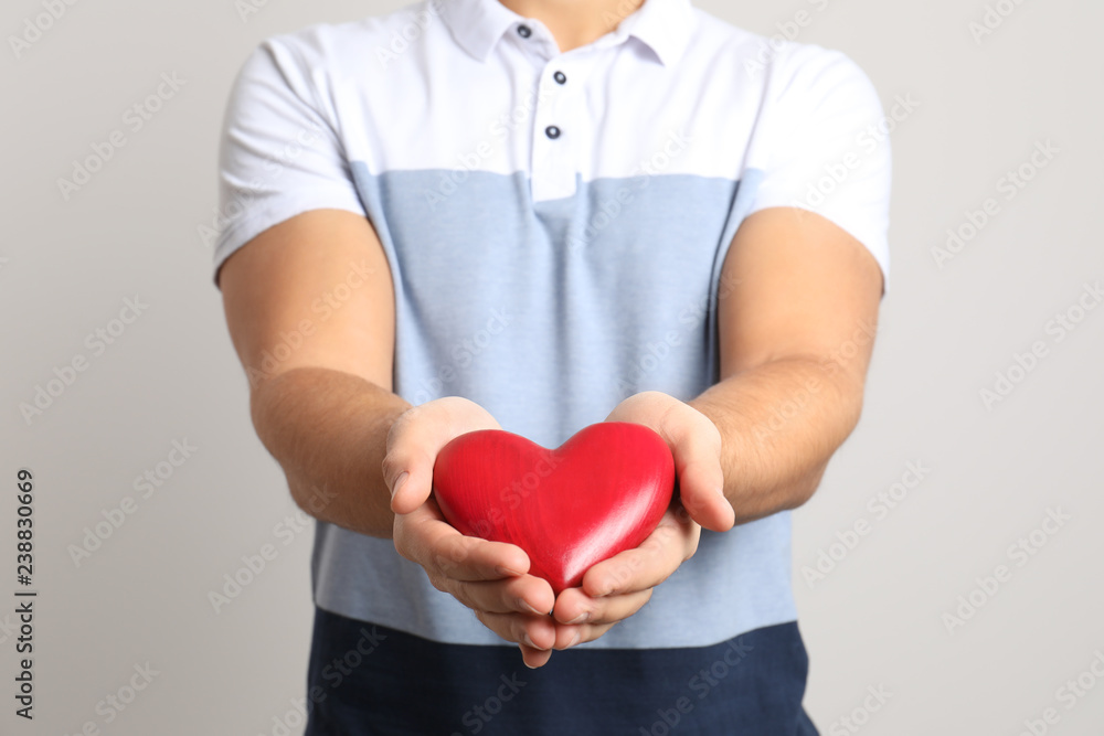 Man holding decorative heart on light background, closeup