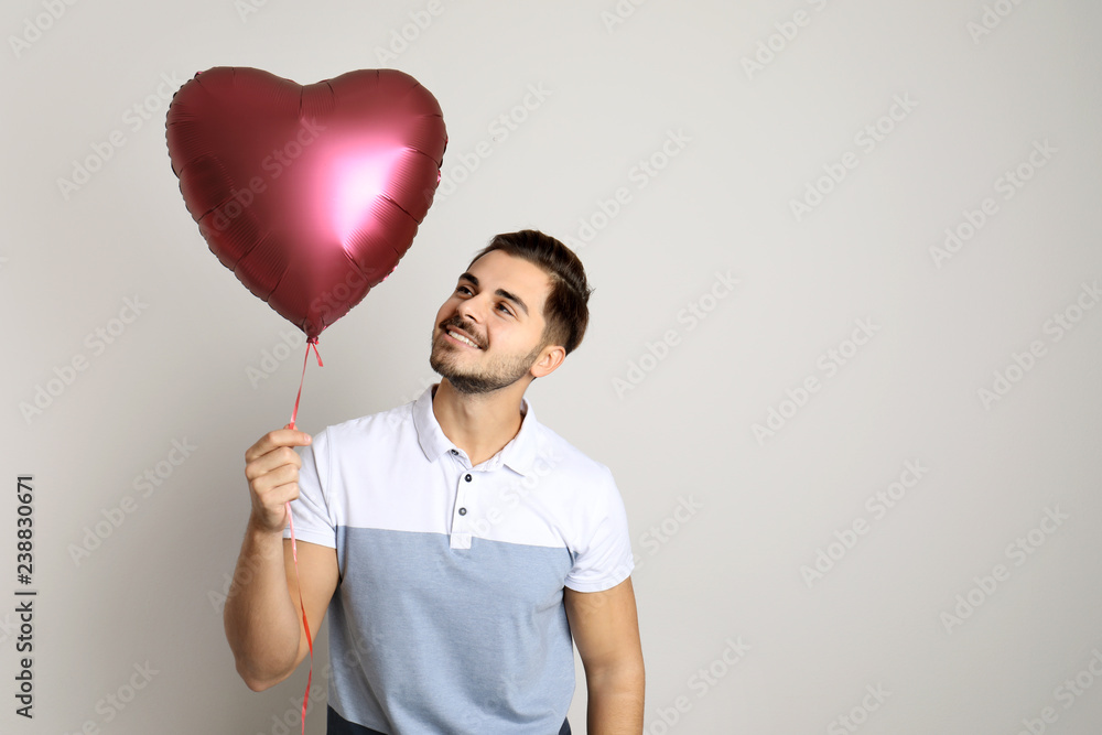 Portrait of young man with heart shaped balloon on light background. Space for text Portrait of young man with heart shaped balloon on light background. Space for text