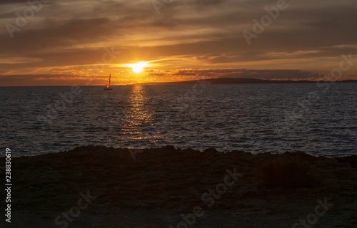 Seascape with sailboat over sunset