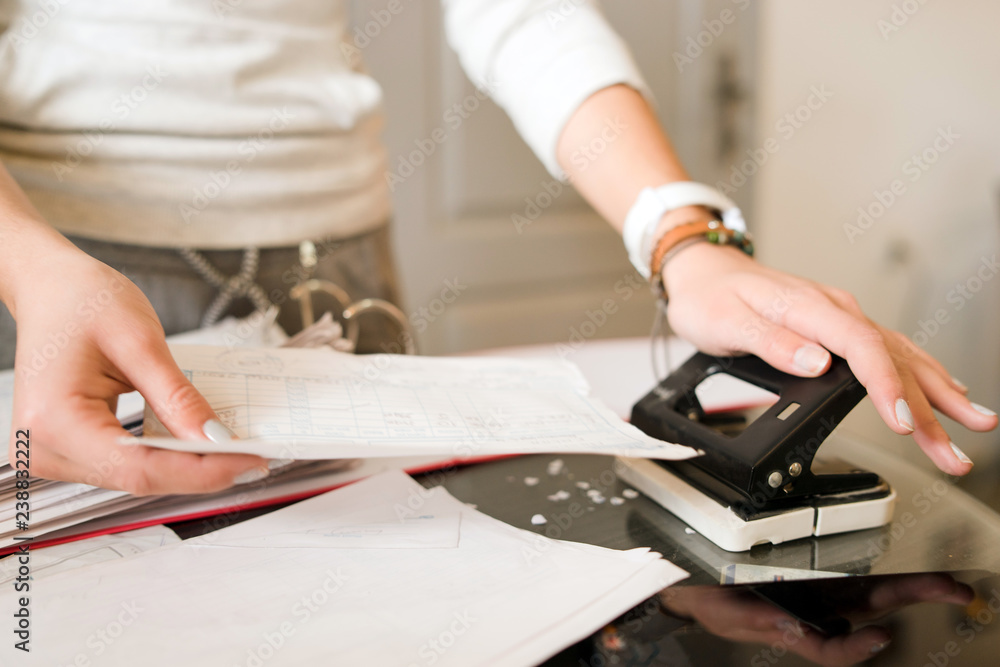 Young woman using punch hole on the documents in the office Young woman using punch hole on the documents in the office