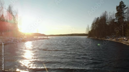 Aerial, drone shot, above a lake, towards a man standing on a rocky shore, near leafless trees, first snow on the ground, near Joensuu, North Karelia, Finland photo