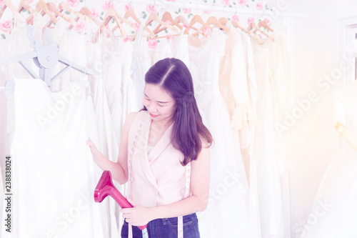 Young owner entrepreneur creative girl textile business sme concept. Portrait beautiful of asian young designer woman work with iron steam in tailor wedding studio, small business workshop. - Image © Pinyaphat