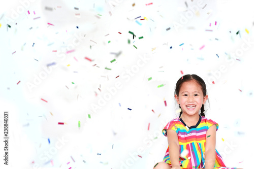 Smiling little Asian kid girl with many falling colorful tiny confetti pieces on white background. Happy New Year or Congratulation Concept.