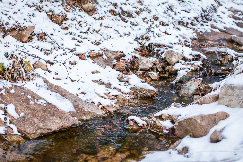 Meltwater stream running through the stones and surrounded by brown melting snow and dry grass at mountains.