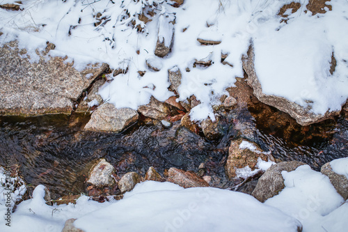 Meltwater stream running through the stones and surrounded by brown melting snow and dry grass at mountains.