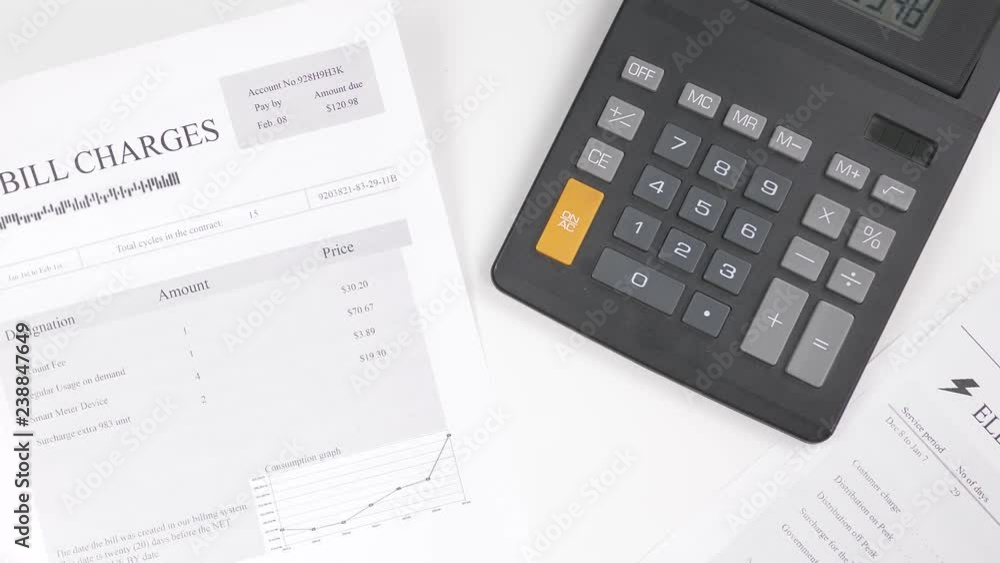 Many utility bills on a table while calculating them all on a calculator. Many utility bills on a table while calculating them all on a calculator.