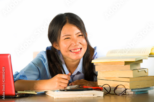 young happy and cute Asian Chinese student girl smiling happy working and studying with texbooks and laptop computer sitting on desk isolated on white background photo