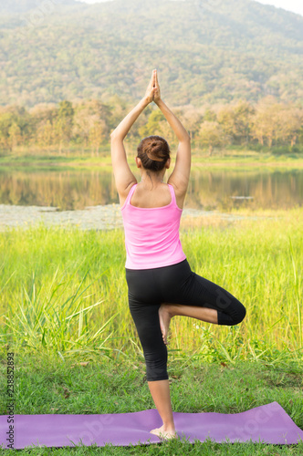Woman practicing yoga tree pose at lake. © peerayot
