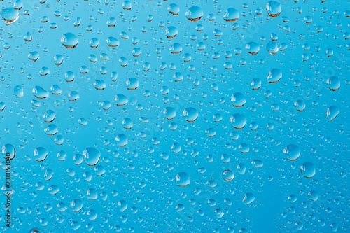 Macro shot of water drops with reflections on a window glass against turquoise blue background