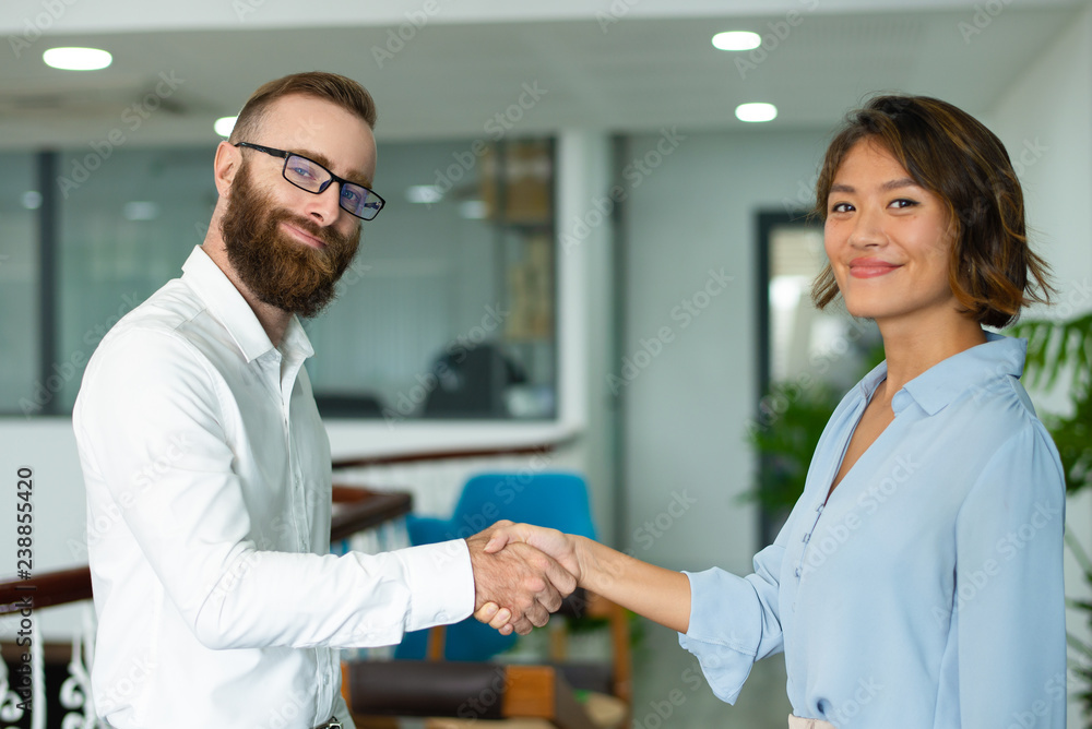 Obraz premium Content confident business partners making handshake and looking at camera. Smiling young multi-ethnic entrepreneur concluding deal. Startup business concept