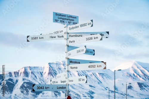 Big pole with directions signs and distances to cities of the world. Blue sky, mountains covered with snow. Longyearbyen, Spitsbergen, Norway