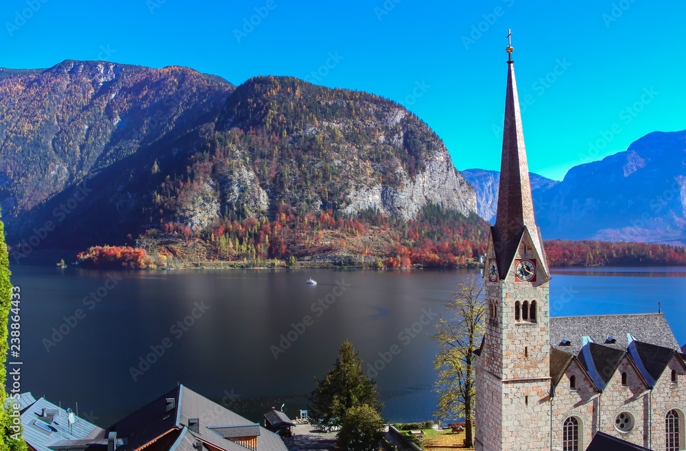 Beautiful landscape on Hallstatt lake with sunrays, blue sky, historic church and mountains