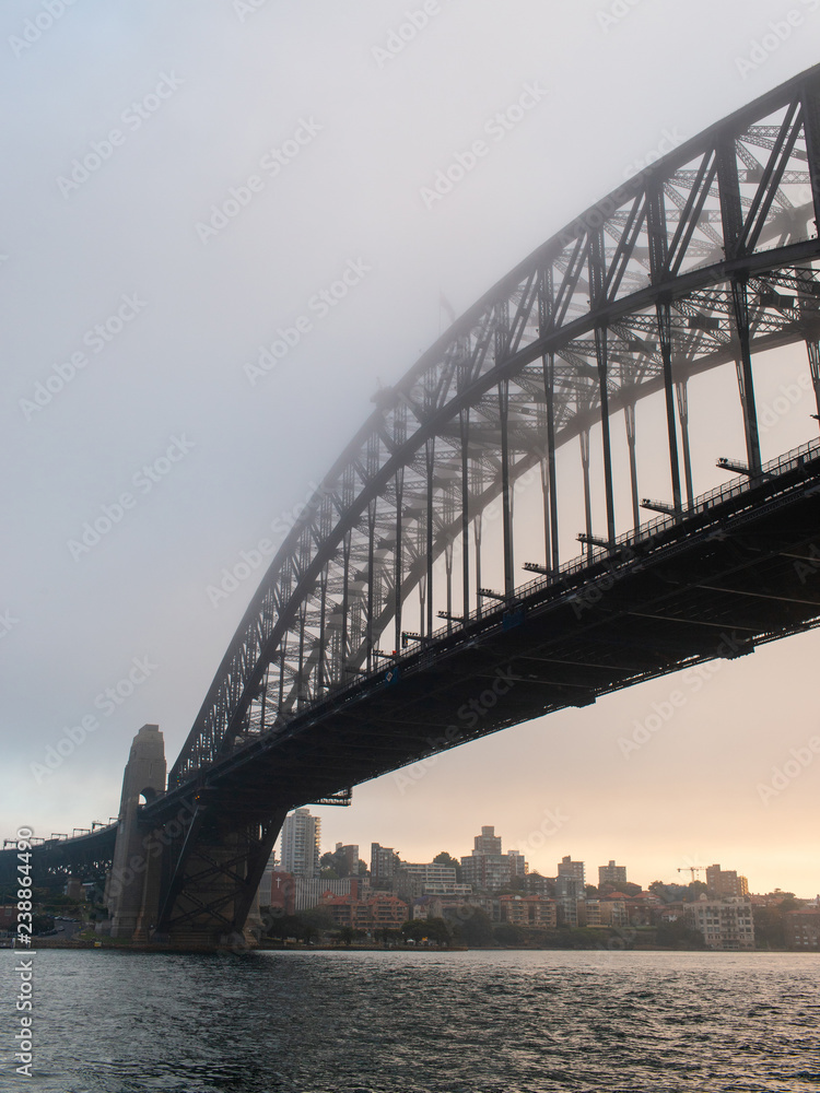 Obraz premium Sydney Harbour Bridge view under sunrise light and fog.