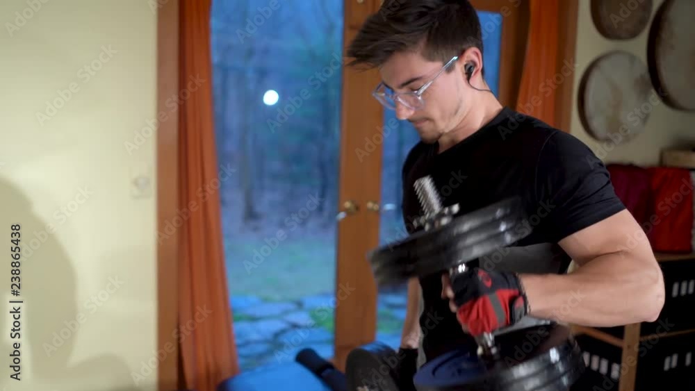 Young bodybuilder hammer curling heavy dumbbells in a home gym