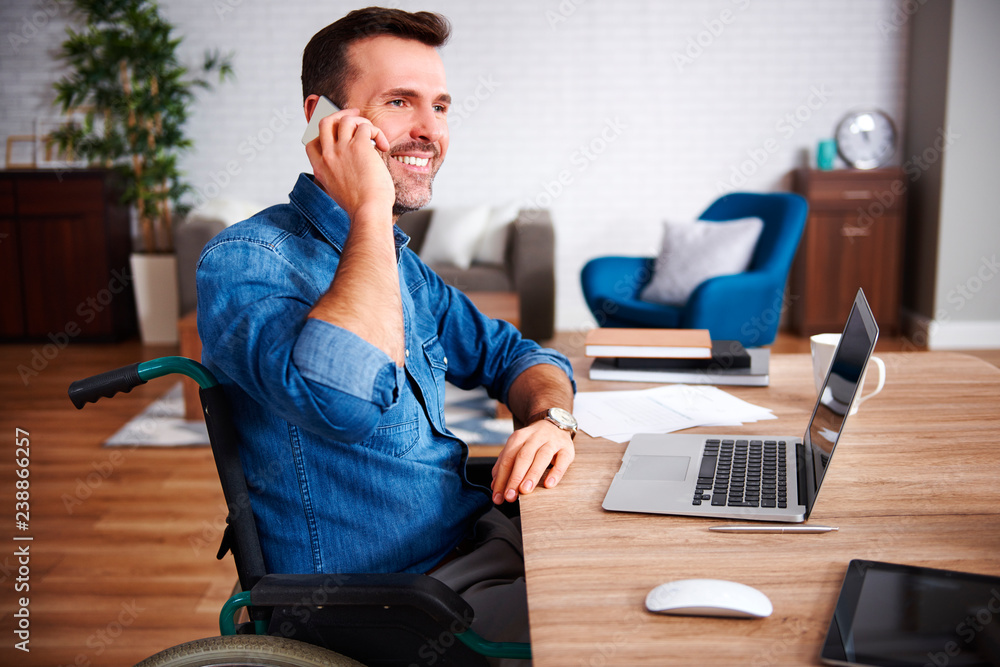 Smiling man on wheelchair talking by mobile phone in home office Smiling man on wheelchair talking by mobile phone in home office