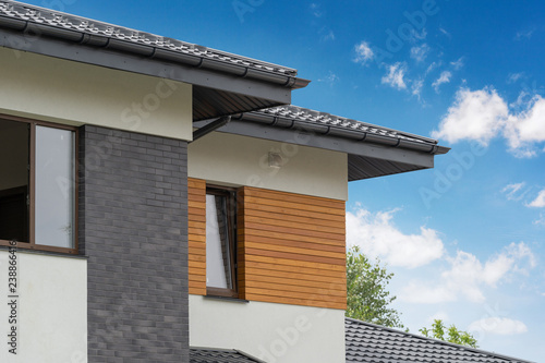Outside photo of beautiful and comfort new house with few apartment and flat room large windows and stone wooden elements on white wall against beautiful sky