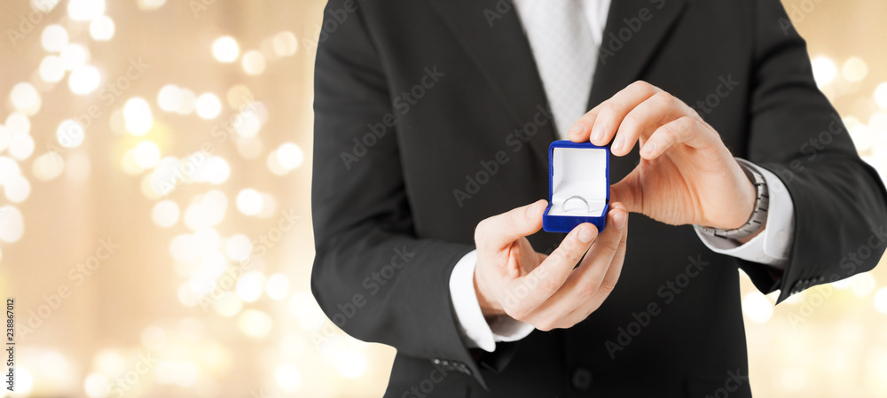 valentines day, proposal and engagement concept - close up of man with diamond ring in little red gift box over festive lights background valentines day, proposal and engagement concept - close up of man with diamond ring in little red gift box over festive lights background