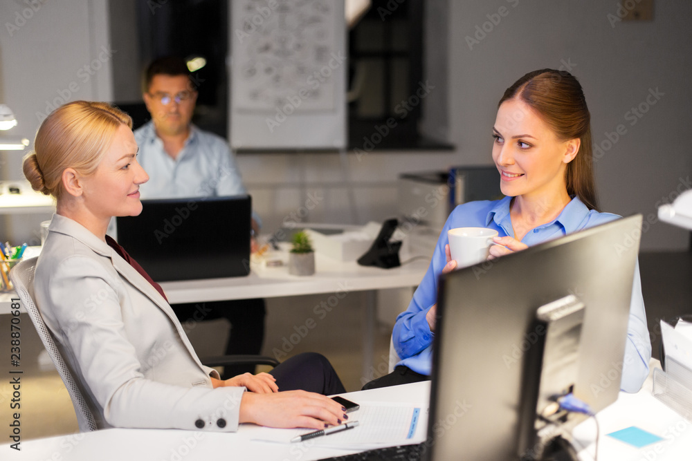 Fototapeta premium business, deadline and communication concept - businesswomen talking and drinking coffee late at night office