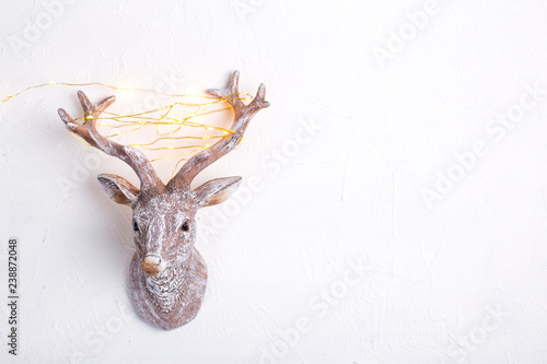 Decorative head of New Year reindeer with fairy light on its antlers on white textured background. photo