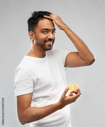 grooming, hairstyling and people concept - smiling young indian man applying hair wax or styling gel over gray background photo