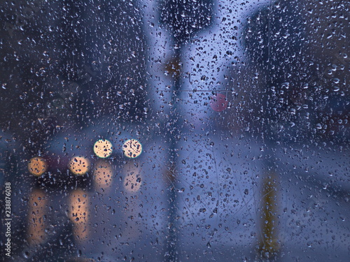 Rain drops on bus stop window and far side visible car lights. Cold rainy day waiting bus stop after work