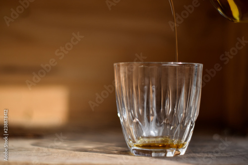 Whiskey drink being poured into a glass against wooden background.