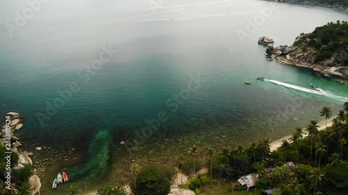 Aerial drone top view of white sand tropical exotic paradise tiny shore in Koh Prangan island, Thailand. Small boats on ocean surface. Cute remote beach with volcanic stones and green coconut palms. photo