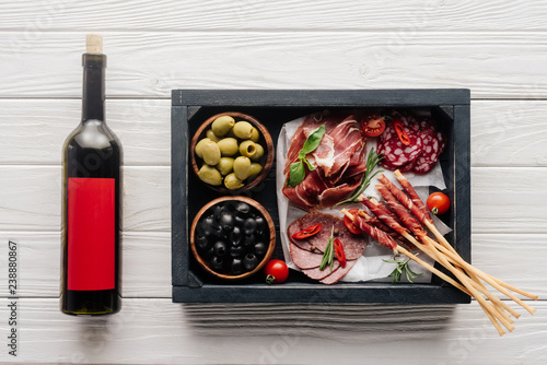top view of bottle of red wine and assorted meat snacks on white wooden tabletop