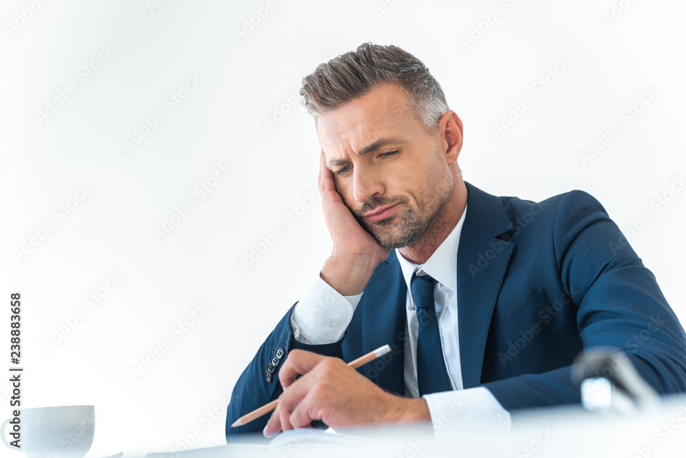 low angle view of tired businessman holding pencil and looking down at table isolated on white low angle view of tired businessman holding pencil and looking down at table isolated on white