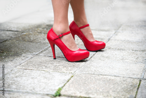 Female legs in bright red shoes with high heels against the pavement tiles background