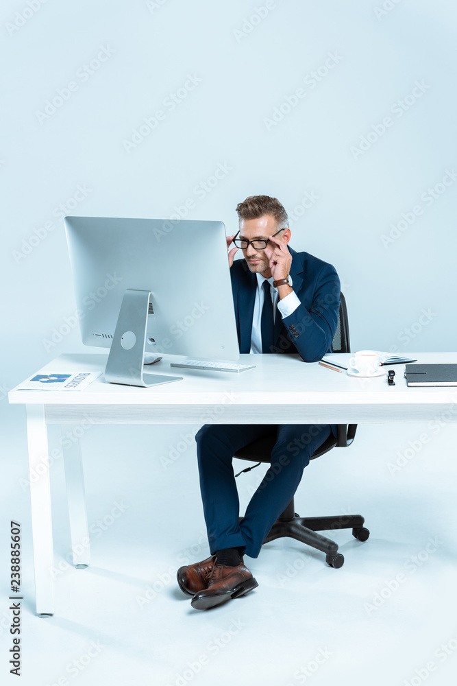 handsome businessman wearing glasses and looking at computer at table isolated on white