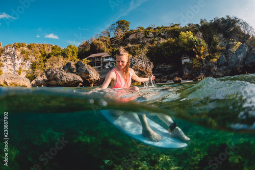 Attractive surfer girl with surfboard. Surfer sit at board in ocean.