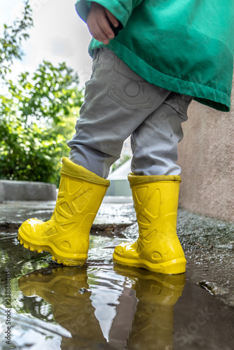 a little boy walks through the puddles in rubber boots in rainy weather