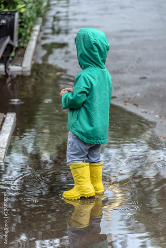 a little boy is standing in a puddle in rubber boots in rainy weather