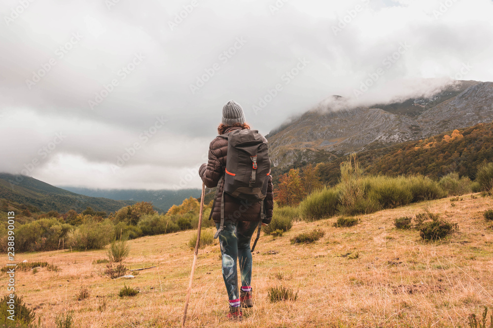 Woman with backpack and cane walking near peak of mountain Woman with backpack and cane walking near peak of mountain