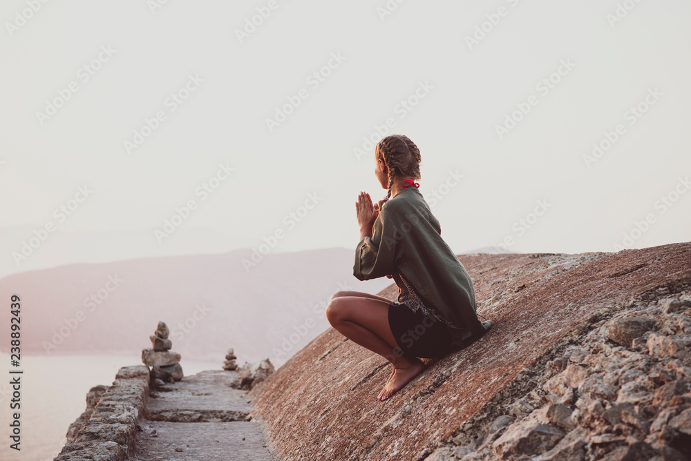 Fototapeta premium Young woman tourist sitting and meditating on ancient stones of Monolithos castle in Rhodes island, Greece, at sunset on clear summer day