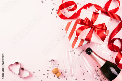 Gift boxes with red ribbon, champagne, two glasses on pink background with de...