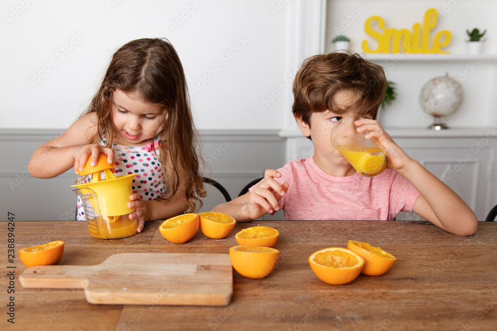 Little girl juicing oranges while brother drinks freshly squized orange juice Little girl juicing oranges while brother drinks freshly squized orange juice