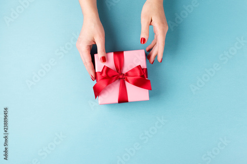 Overhead view on female hands with pink gift box wrapped with red bow on blue...