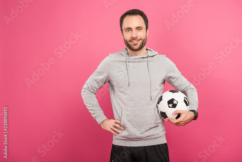 handsome football player holding ball isolated on pink