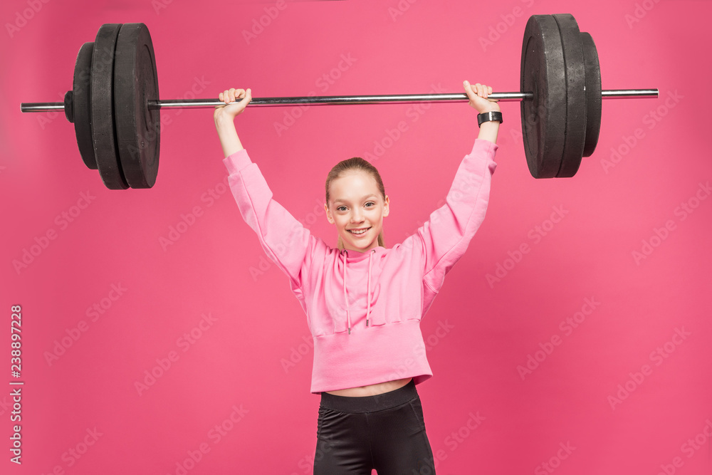 athletic female preteen working out with barbell, isolated on pink athletic female preteen working out with barbell, isolated on pink